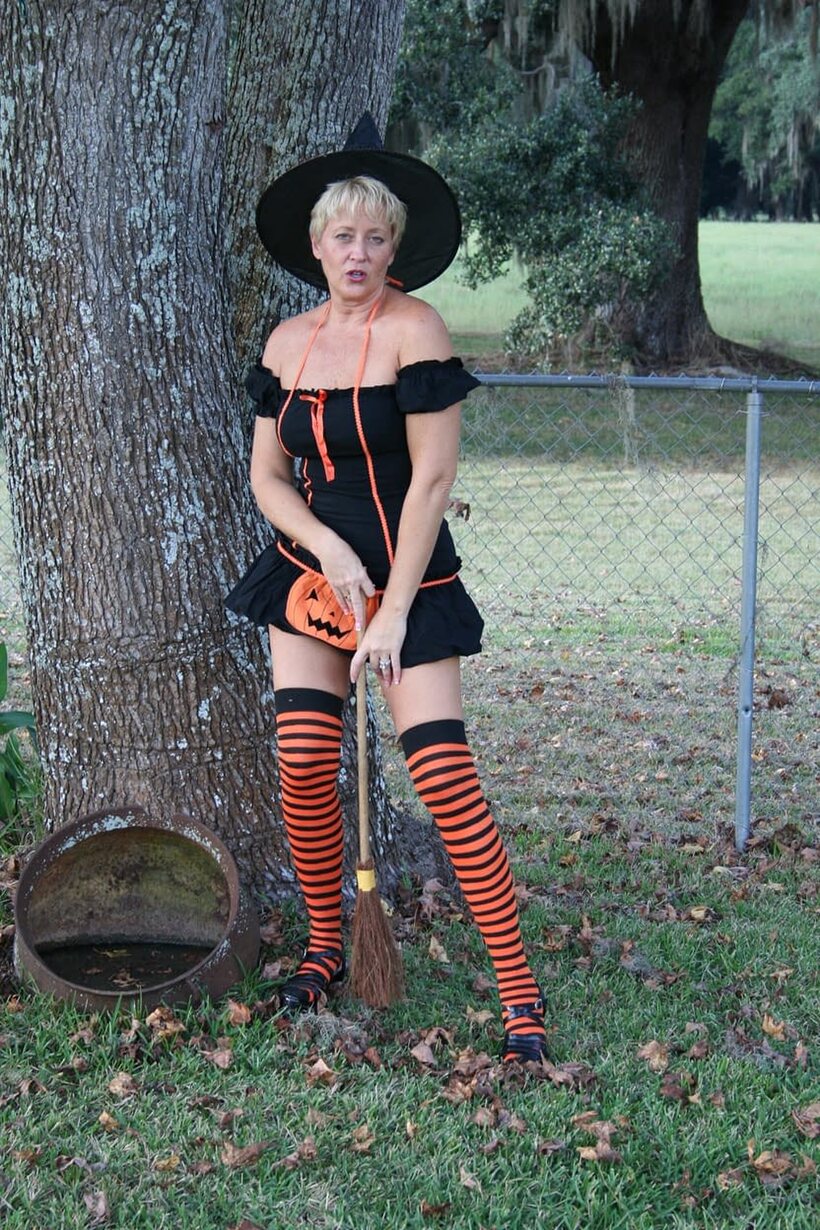 Image 4/20: Outdoors in a Halloween costume, Tracy Lick teases her ass with a broom