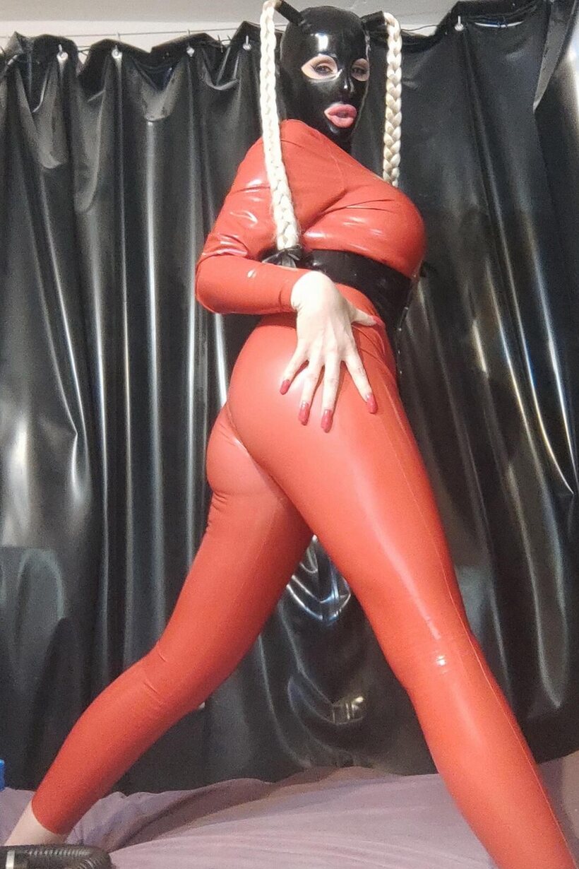 Image 16/16: Long braided pigtails frame her ass in tight latex