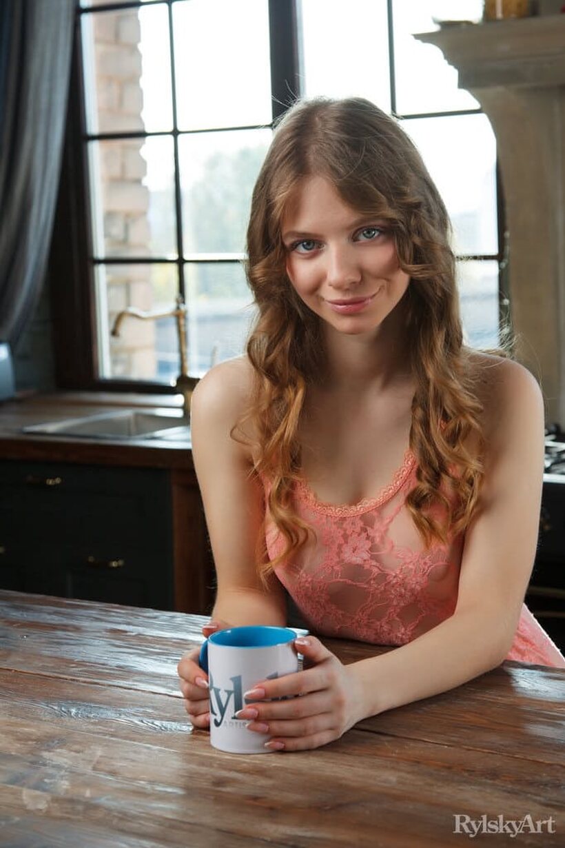 Image 1/16: Naked on the kitchen table, Siya poses beside a cup of coffee