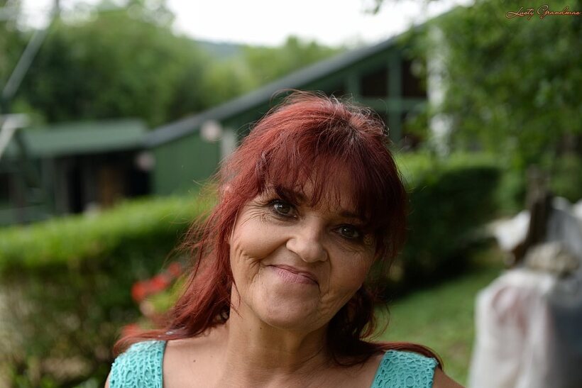 Image 5/16: Livia, a redhead granny, hikes her blue dress to show natural tits