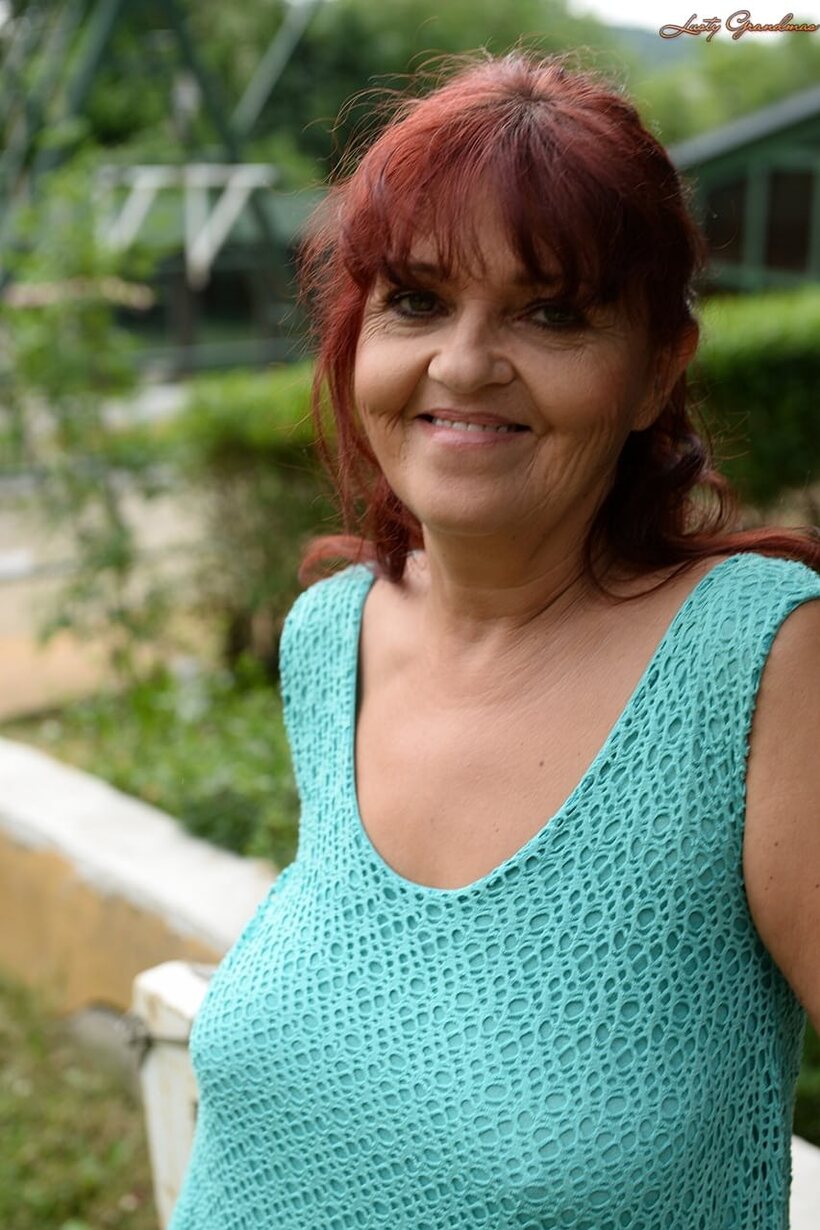 Image 7/16: Livia, a redhead granny, hikes her blue dress to show natural tits