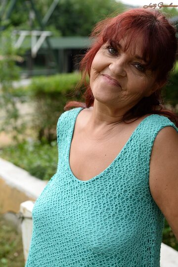 Livia, a redhead granny, hikes her blue dress to show natural tits